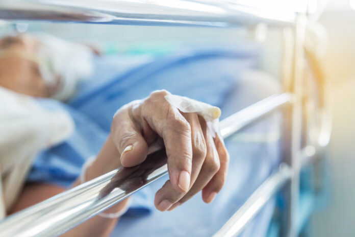 Close up hand of elderly patient with intravenous catheter for injection plug in hand during lying in hospital ward room
